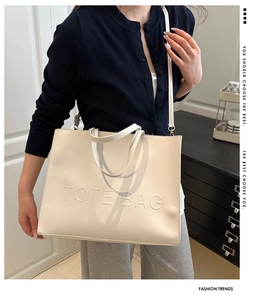 Fashionable beige large tote bag with embossed letters shown on a female model
