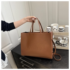 Lifestyle shot of large brown tote bag with embossed letters and shoulder strap