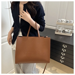 Close-up of the embossed TOTE BAG text on a textured brown leather tote bag