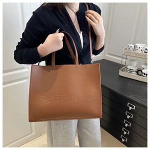 Detail of a brown textured tote bag with embossed lettering and adjustable shoulder strap