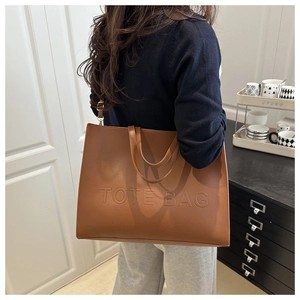 Detail of embossed TOTE BAG lettering on brown textured leather tote with shoulder strap