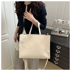 Detail of embossed TOTE BAG lettering on cream large capacity textured leather handbag