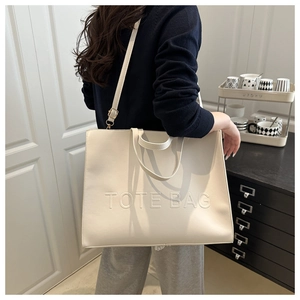 Detail of cream white tote bag featuring embossed logo and premium faux leather texture