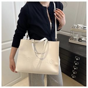Detailed view of the embossed TOTE BAG lettering on a cream faux leather tote bag