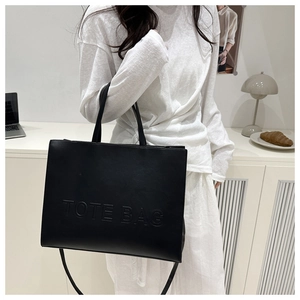 Detail of black leather tote bag with embossed TOTE BAG lettering and long shoulder strap