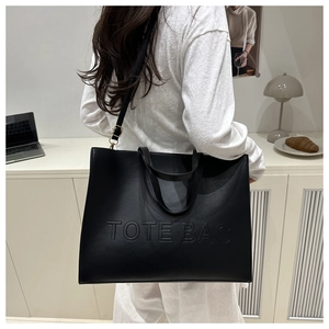 Close-up of black textured leather tote bag with embossed lettering and shoulder strap
