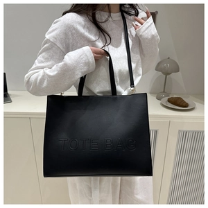 Detail of embossed TOTE BAG lettering on black leather tote with adjustable shoulder strap