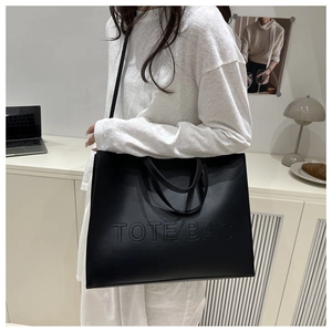 Detail of black faux leather tote bag with embossed TOTE BAG text in a lifestyle setting