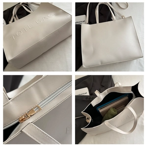 Detail view of large cream tote bag with embossed letters and metal zipper closure