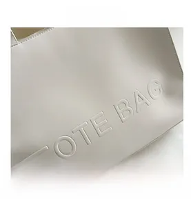 Detail of white leather tote bag featuring embossed lettering and fine stitching texture