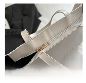Detail of smooth gold zipper closure and BAG embossed texture on beige tote bag
