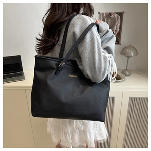 Detail of cross-grain black tote bag with gold fashion lettering on a shoulder strap