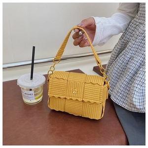 Detail of yellow woven texture with golden floral buckle on small square shoulder bag