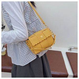 Detail of yellow woven crossbody bag with gold flower buckle and chain strap