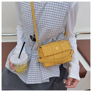 Close-up of yellow woven crossbody bag featuring a golden flower clasp and chain strap
