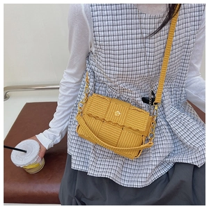 Close-up of yellow woven crossbody bag featuring scalloped edges and floral metal buckle