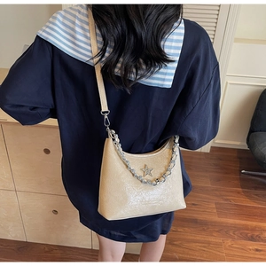 Détail d'un sac baguette en cuir laqué beige avec chaîne argentée et logo étoile à l'épaule