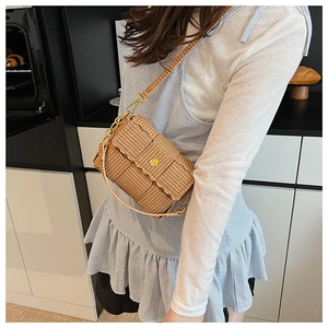 Detail view of woven straw crossbody bag featuring a golden flower clasp and chain strap
