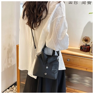 Macro detail of black jacket-shaped crossbody bag featuring silver buttons and leather strap