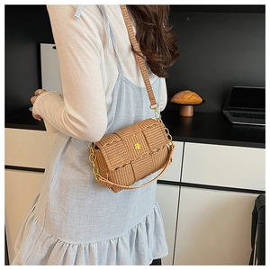 Detail of woven straw crossbody bag featuring golden flower buckle and chain strap