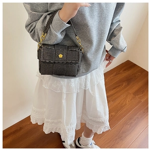 Detail of woven square bag in dark brown with elegant gold floral clasp and metal rings