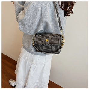Detail of grey woven texture shoulder bag with gold floral clasp on a model