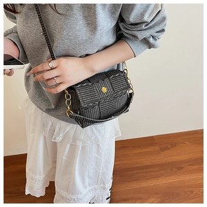 Detail of black woven crossbody bag featuring a golden petal-shaped lock and chain strap