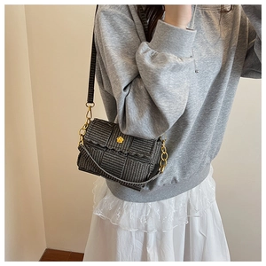 Detail of dark grey woven square bag with golden camellia clasp and chain strap