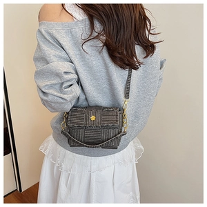 Detail of woven square bag with gold flower buckle and chain strap on model