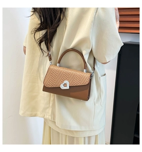 Detail of woven straw texture and silver heart lock on a brown crossbody bag