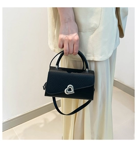 Close-up of black crossbody bag featuring a silver heart-shaped lock and top handle