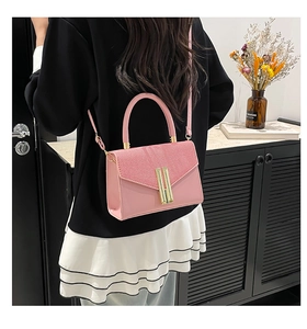 Pink crossbody bag with woven texture flap and golden metal clasp on a stylish model