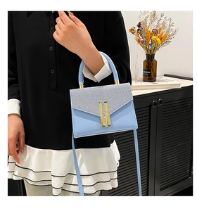 Detail of light blue structured crossbody bag featuring textured panels and gold buckles