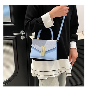Detail of light blue crossbody bag with woven texture lid and golden rectangular metal lock