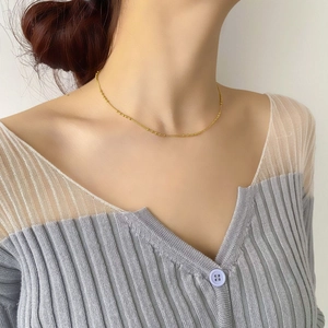 Collier minimaliste en perles dorées porté par un mannequin avec gilet gris