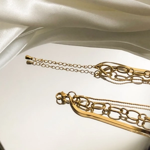 Detail of layered gold necklaces with snake and oval link chains on white silk background