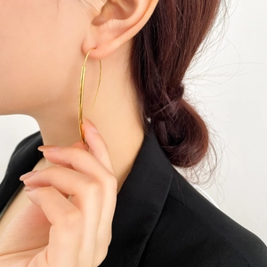 Dettaglio di orecchini pendenti lineari dorati indossati da una modella in nero