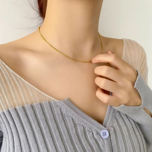 Gros plan d'un collier chaîne à perles dorées porté avec un élégant pull en maille
