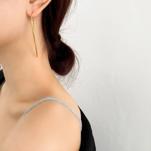 Dettaglio di eleganti orecchini lunghi a ago dorati indossati da una modella