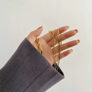 Close-up of layered gold chains including chunky link and flat snake bone necklaces