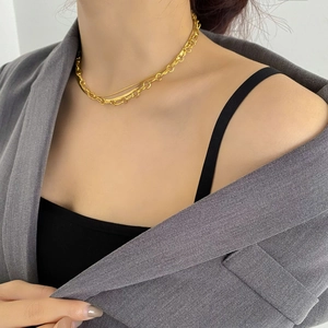 Close-up of layered gold snake chain and curb link necklace worn with a blazer