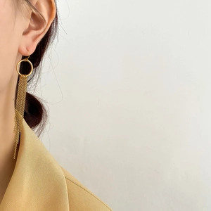 Gros plan de boucles d'oreilles pendantes dorées portées avec un blazer beige