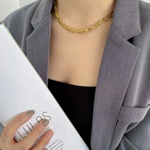 Detail of layered gold link chain necklace worn with a stylish dark gray blazer