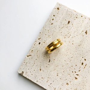 Dettaglio dell'anello dorato a doppio strato minimalista su pietra travertino
