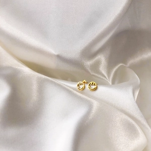 Gros plan détaillé des boucles d'oreilles smiley dorées sur fond de soie blanche