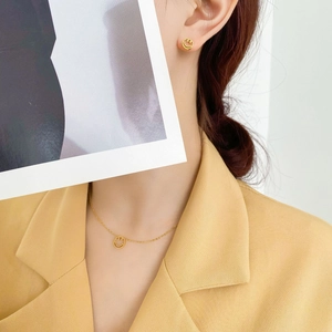 Ensemble collier et boucles d'oreilles dorés avec pendentif smiley porté par un mannequin