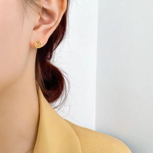 Gros plan d'un modèle portant une puce d'oreille smiley dorée ajourée aux bords texturés
