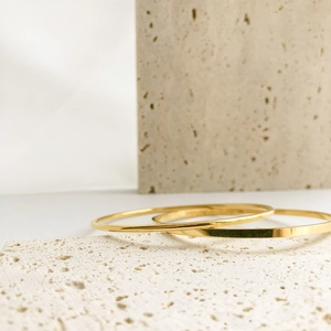Minimalist gold-plated stainless steel bangles set on a natural stone background