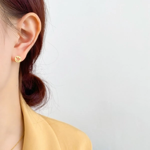 Gros plan d'une boucle d'oreille dorée avec un visage souriant évidé minimaliste