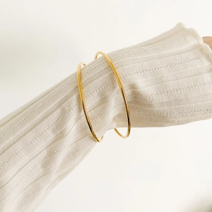 Polished gold plated titanium steel bangles shown on a textured white knit sleeve